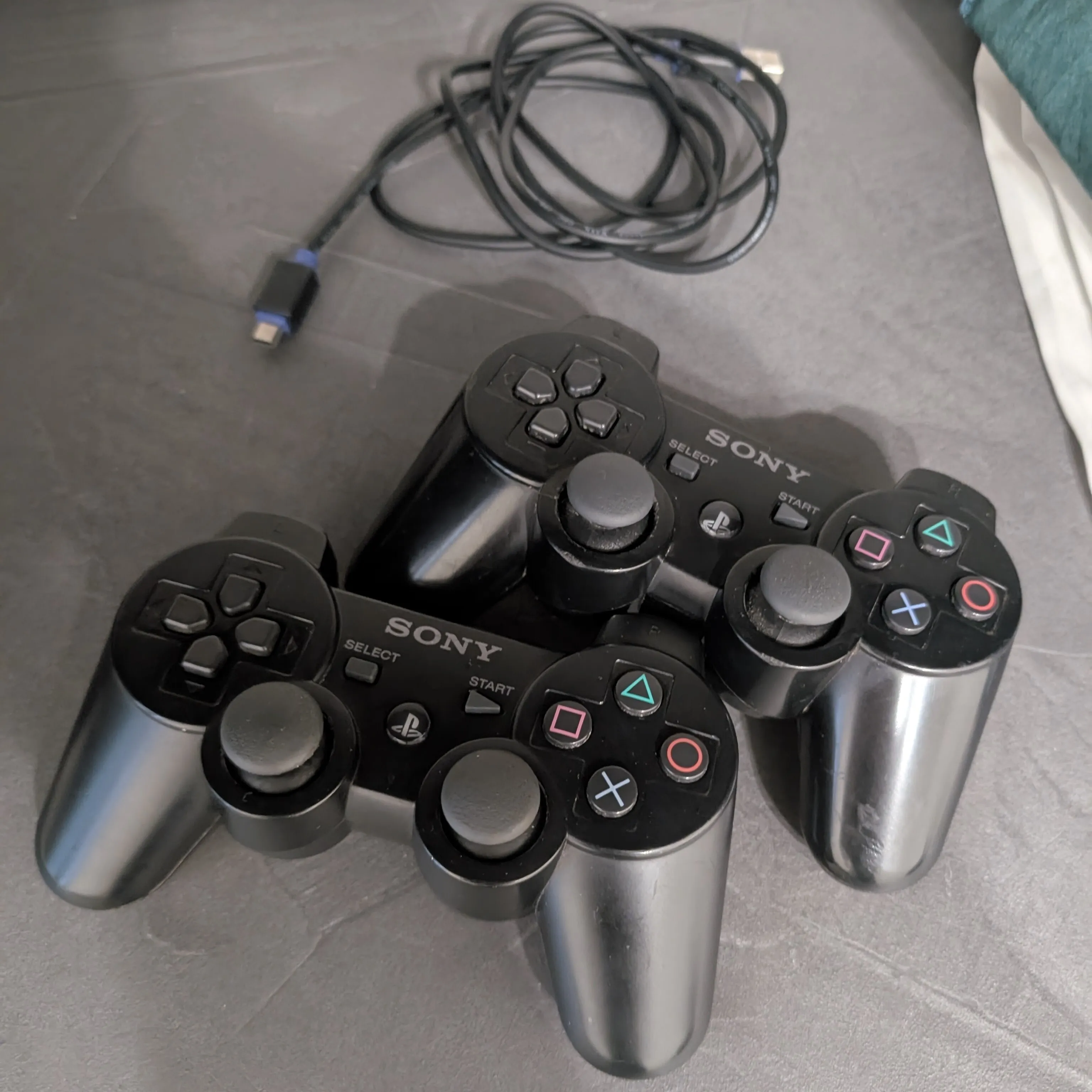 Close-up shot of the sourced DualShock 3 pads. In the background you can also see the cable that I received with said controllers.